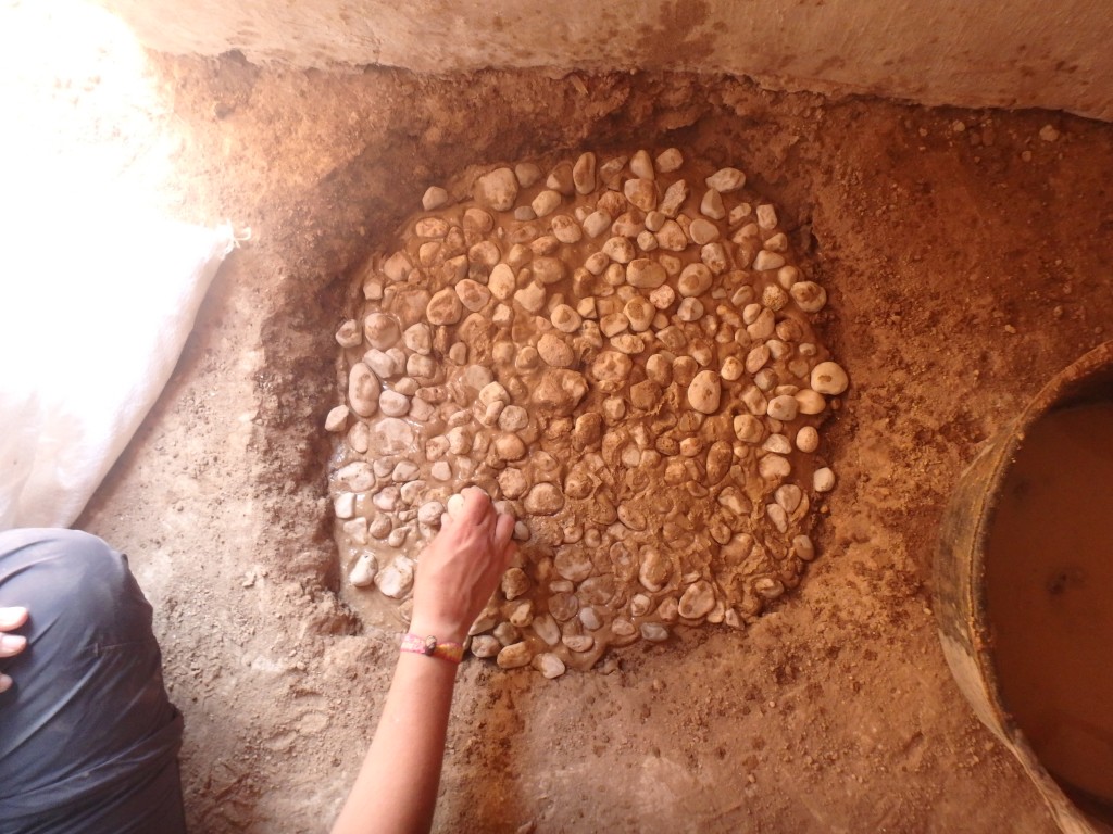 Construcció experimental d’una llar protohistòrica, en un espai interior, excavant una cubeta de pocs centímetres de fondària i reblerta amb capes de fang i còdols. Foto: projecte TRANSCOMB (ICAC).